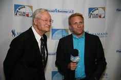 two men standing next to each other in front of a white wall holding microphones