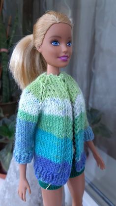 a doll with blonde hair and blue eyes wearing a colorful sweater in front of a window