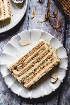 a slice of cake on a plate with almonds next to it and another piece of cake in the background