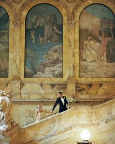 a man in a tuxedo is standing on the stairs next to some paintings