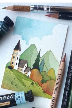 watercolor pencils and markers are sitting on a paper with a drawing of a house in the background