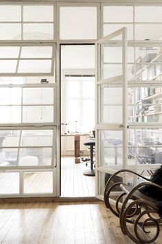 an open glass door leading to a room with wooden floors and white walls, along with a rocking chair in the foreground