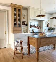 a kitchen with wooden floors and white cabinets is shown in this image, there are two stools at the center of the island