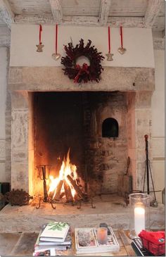 a fireplace with a wreath on the mantle and fire in it, surrounded by books