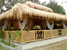 a tiki hut with thatched roof and white drapes on the porch area