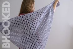 a woman holding up a crocheted shawl in front of a white wall