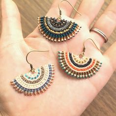 two pairs of multicolored beaded earrings on a person's hand