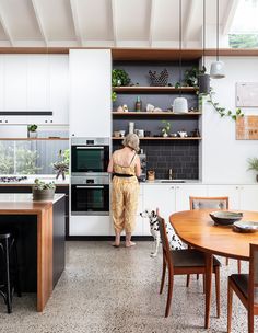 a woman standing in a kitchen next to a table with chairs and an oven on it