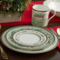 a table set with plates, silverware and a potted plant in the background