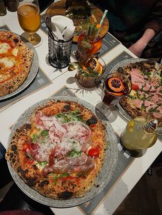 two pizzas sitting on top of metal pans next to glasses and drinks in front of them