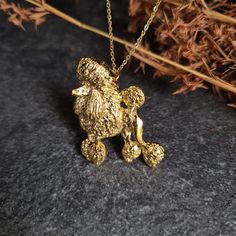 a gold teddy bear pendant is sitting on a black surface next to some dry grass