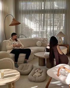 a man and woman sitting on couches in a living room next to a window