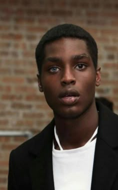 a young man in a black suit and white t - shirt looking at the camera