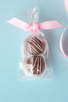 two chocolate covered candies wrapped in cellophane and tied with a pink ribbon