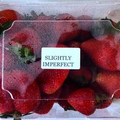 a plastic container filled with lots of ripe strawberries next to a sign that says slightly imperfect