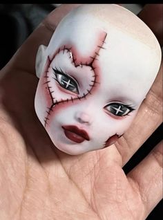 a hand holding a fake doll with makeup on it's face