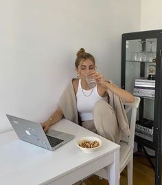 a woman sitting at a table with a laptop drinking water