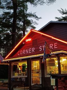 the corner store is lit up with red and white lights at night, in front of some trees