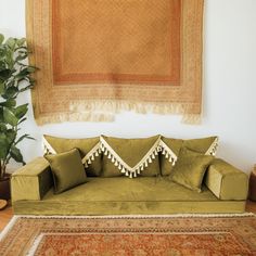 a green couch sitting on top of a wooden floor next to a rug and potted plant