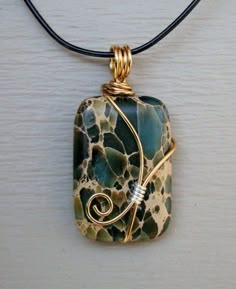 a necklace with a pendant made out of glass and gold wire on a black cord