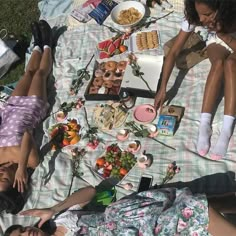 two people laying on a blanket with food and drinks in the grass next to each other