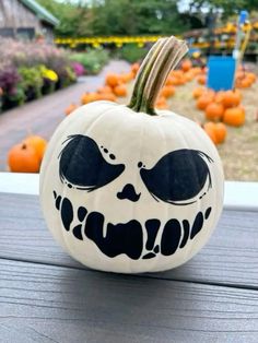 a white pumpkin with black eyes and mouth painted on it's face, sitting on a porch