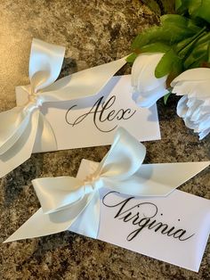 three place cards with white flowers and green leaves in the background on a granite countertop