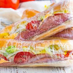 two sandwiches wrapped in plastic sitting on top of a table