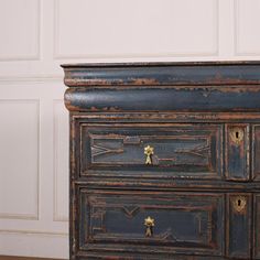 an old black dresser with gold handles and knobs on the bottom drawer, in front of a white wall