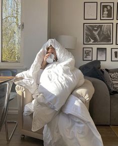 a woman wrapped up in a blanket and holding a coffee cup while sitting on a couch