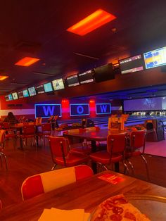 a bowling alley filled with lots of tables and chairs next to neon signs on the wall