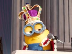 a minion wearing a crown and holding a microphone in front of a podium with two microphones