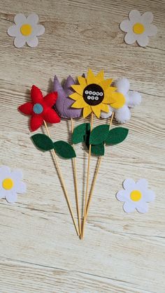 three felt flowers sitting on top of wooden sticks