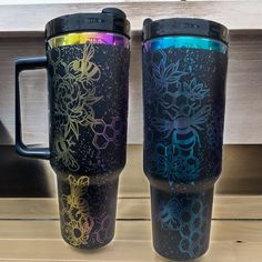 two travel mugs sitting next to each other on top of a wooden countertop