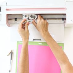 two hands are working on an appliance that is attached to a wall mounted air conditioner