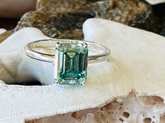 an emerald colored ring sitting on top of a rock