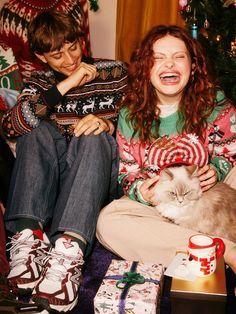 a woman sitting on the floor with a cat in her lap and presents around her