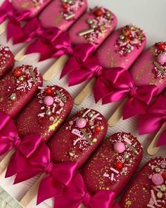 pink and gold decorated cookies on sticks in a box with bows around the edges, ready to be eaten