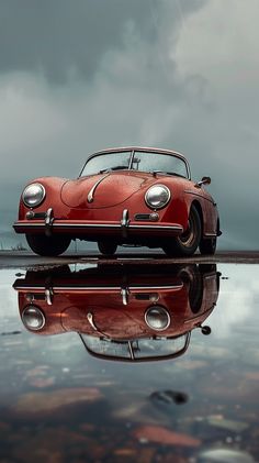 an old red car sitting on top of a body of water under a cloudy sky