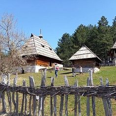 an old wooden fence in front of two small houses with thatched roofs and trees