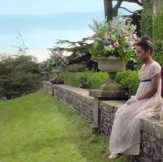 a woman in a white dress sitting on a stone wall next to a flower pot