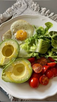 an avocado, tomato, egg and lettuce on a white plate