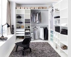 a white closet filled with lots of clothes and shoes next to a chair on top of a shaggy rug