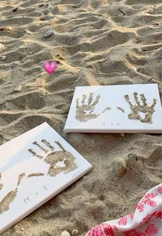 two handprints are placed on the sand next to a towel and pink heart