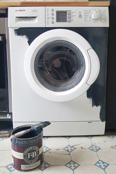 a white and black washer sitting next to a can of paint on the floor