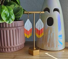 a pair of beaded earrings sitting on top of a wooden stand next to a potted plant