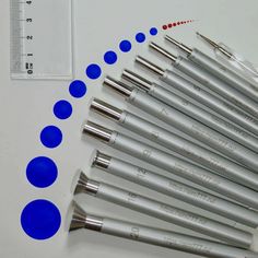 a group of blue and silver pens lined up next to a thermometer on a white surface