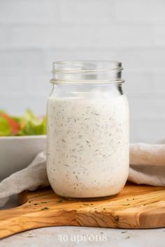 a jar filled with dressing sitting on top of a wooden cutting board next to a salad