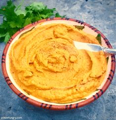 a bowl filled with hummus and parsley on top of a table next to a knife