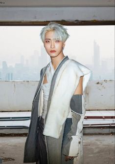 a woman with white hair wearing a gray and white outfit in front of a cityscape